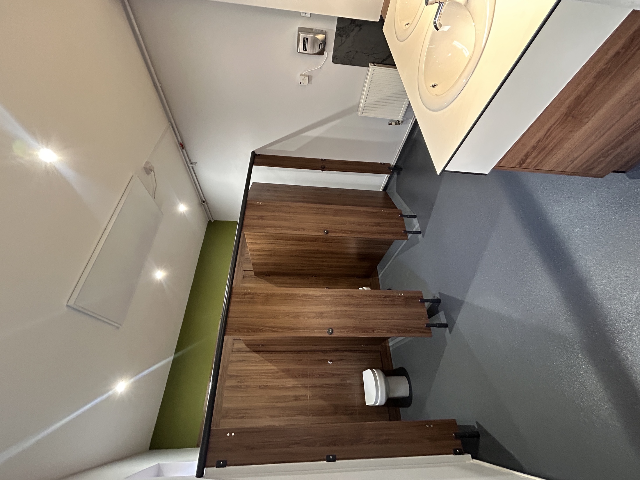 Completed commercial washroom with walnut-effect cubicles, twin basins and a durable grey floor.