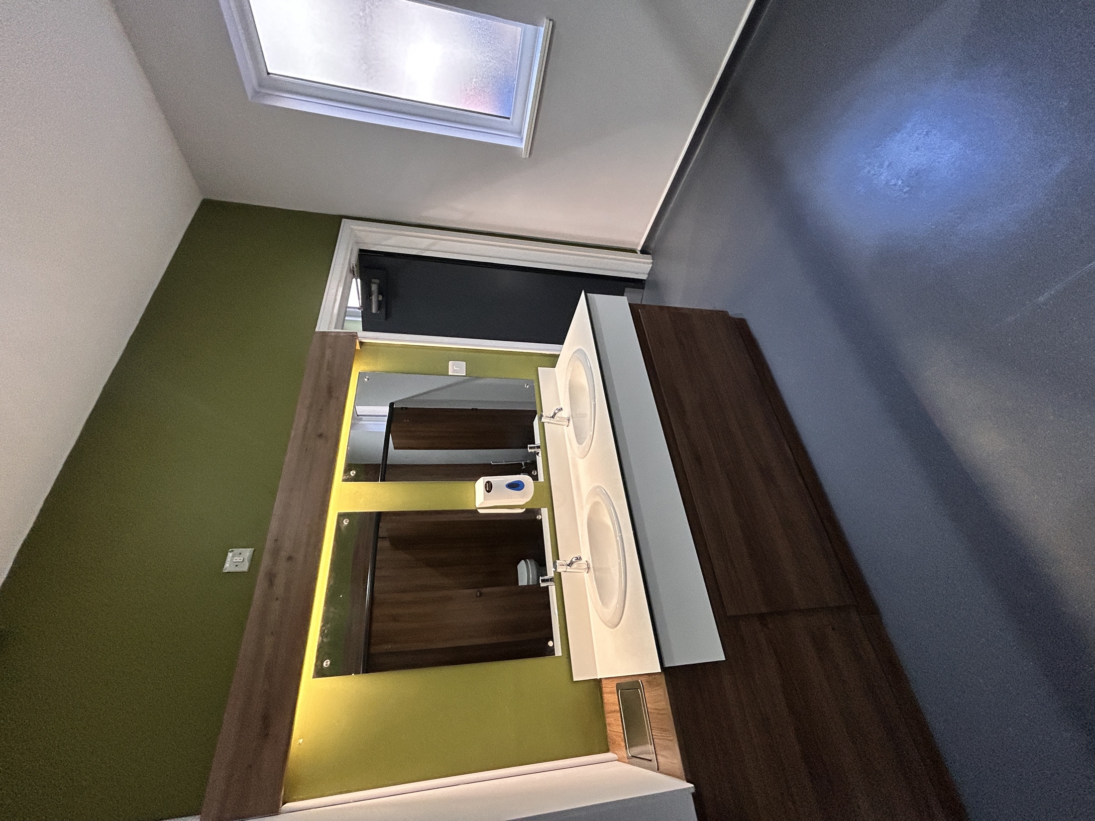 A completed commercial washroom with a double vanity, illuminated mirrors and a green feature wall.