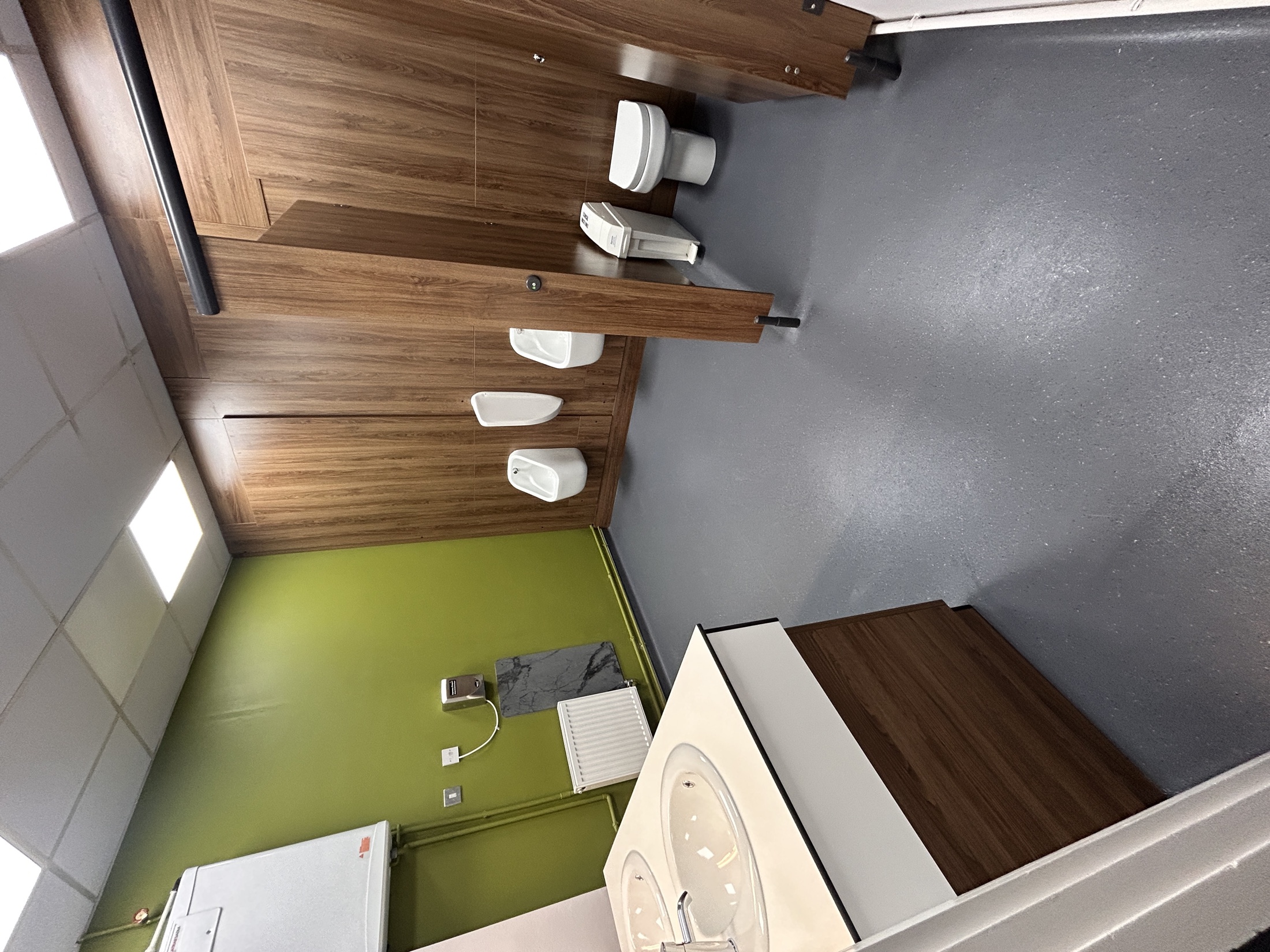 Commercial washroom with coordinated walnut-effect cubicles, urinals and a shared basin.