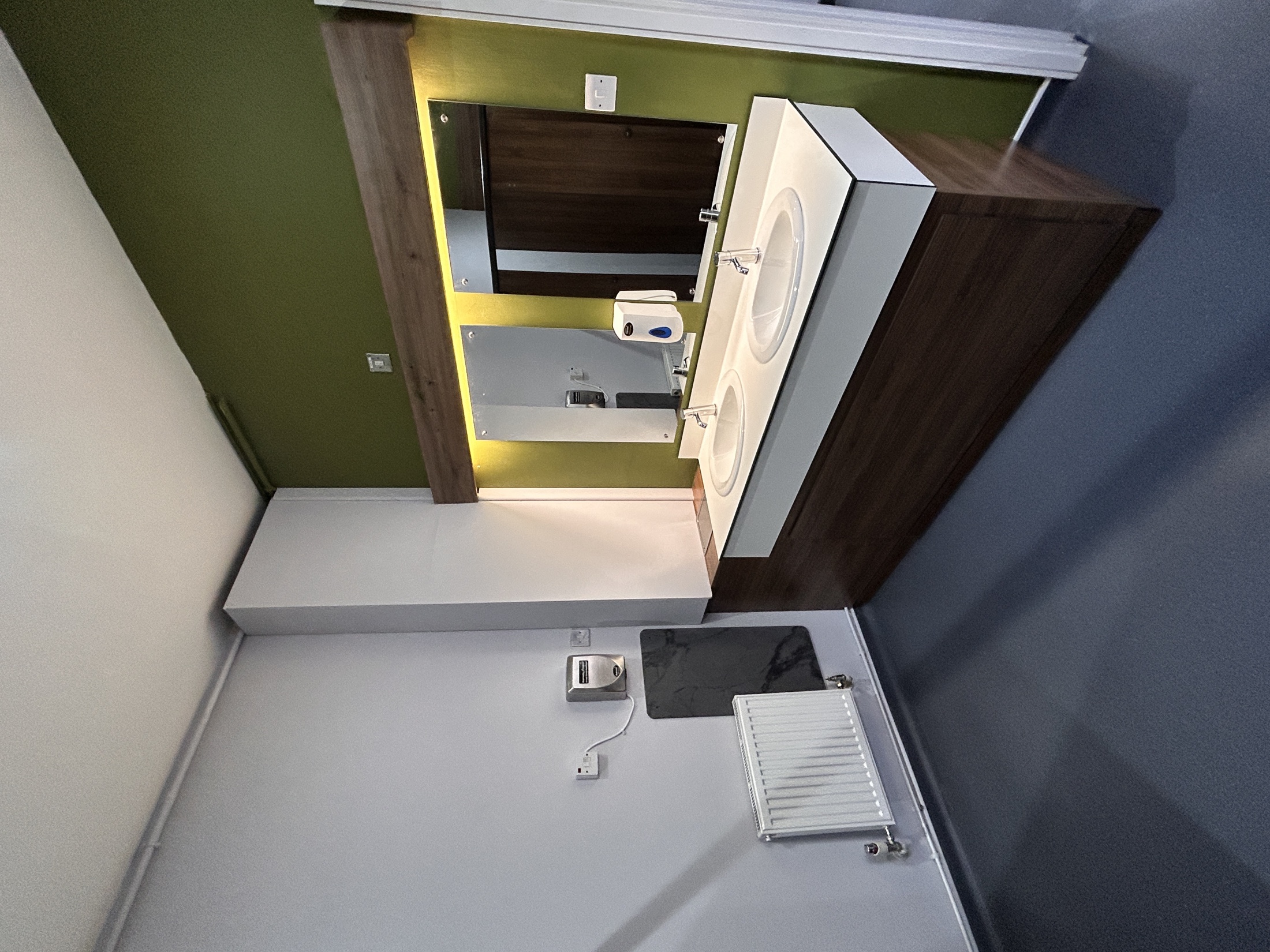 Double commercial vanity with illuminated mirrors, walnut-effect joinery and a green feature wall.