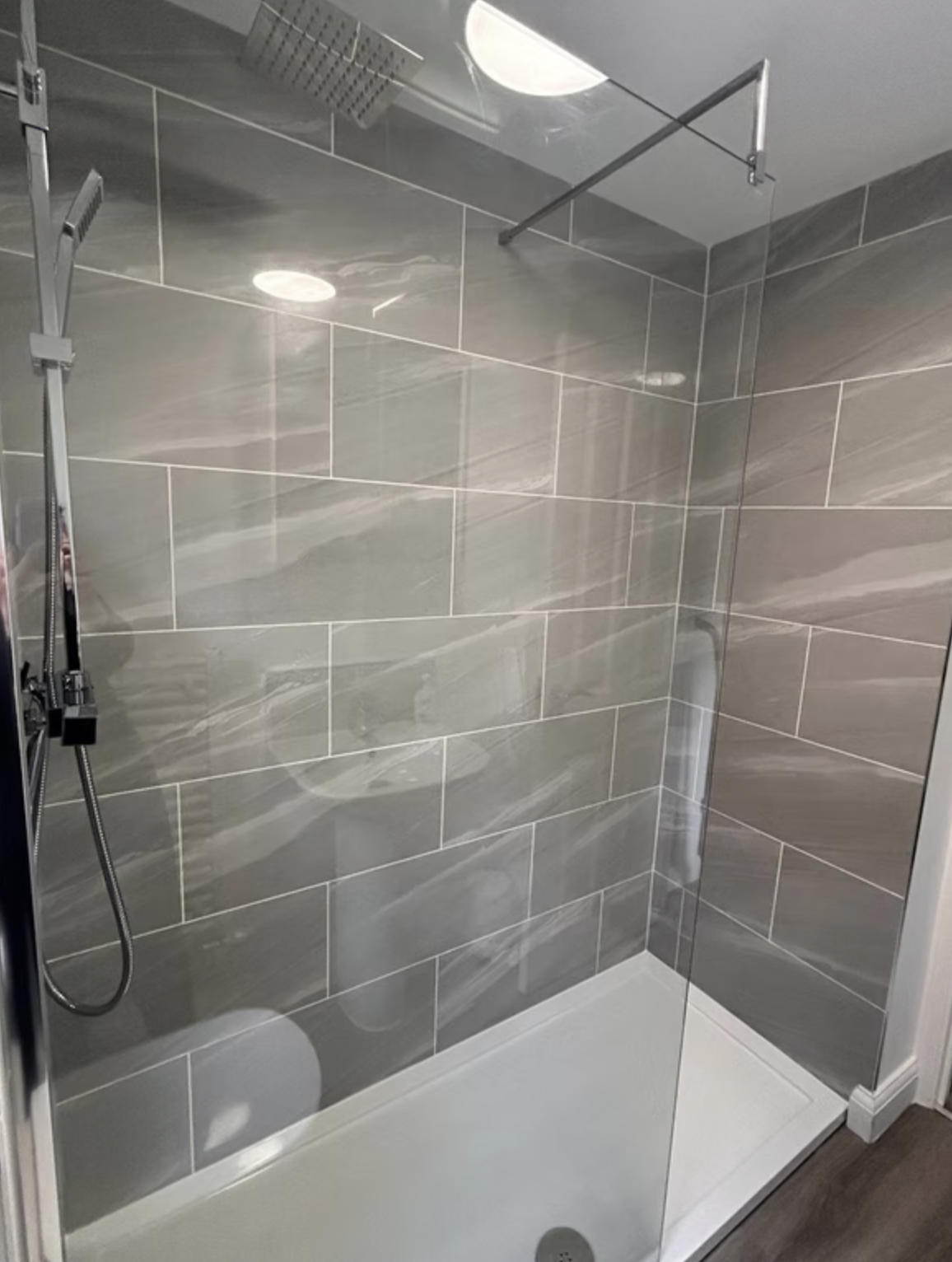 A walk-in shower in grey marble-effect porcelain with chrome rainfall head and a fixed glass screen.