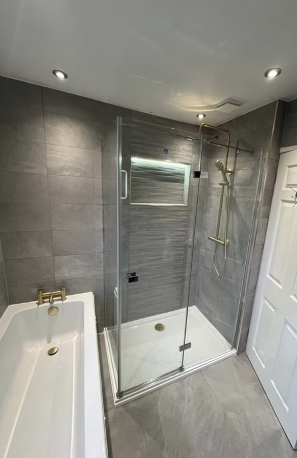 A grey wave-textured shower with brushed brass rainfall head and frameless glass.