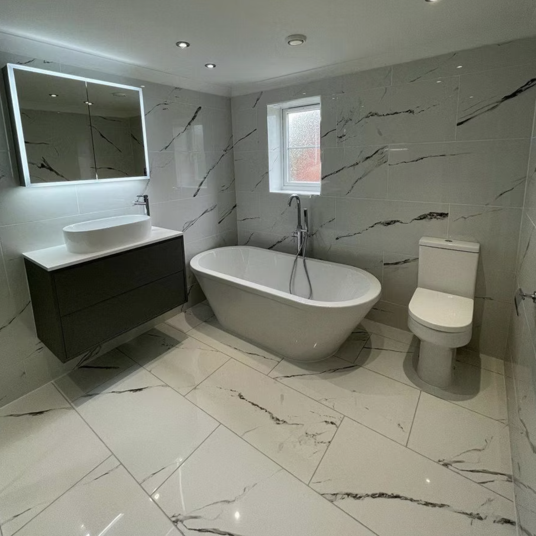 The Marble Bathroom: freestanding bath and grey wall-hung vanity in marble-effect porcelain.