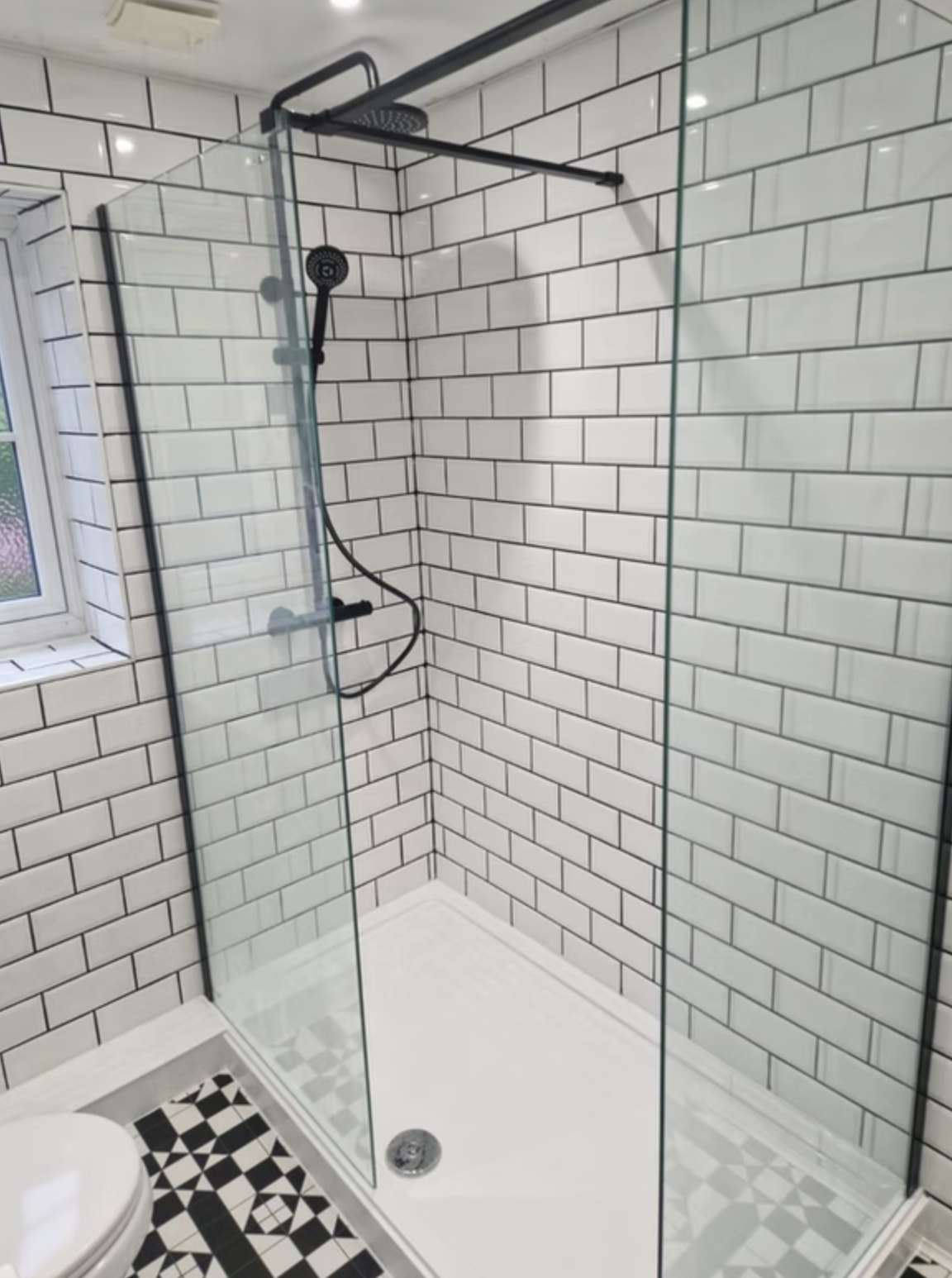 A wide level shower with sliding glass, white metro tiles and a rainfall head.