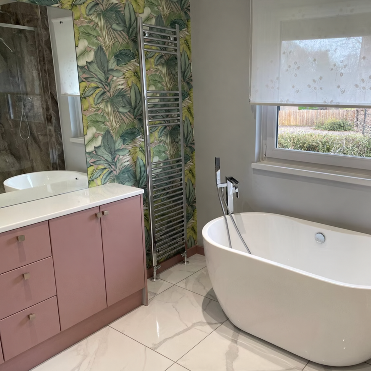 A freestanding oval bath beside a botanical feature wall and walk-in shower.