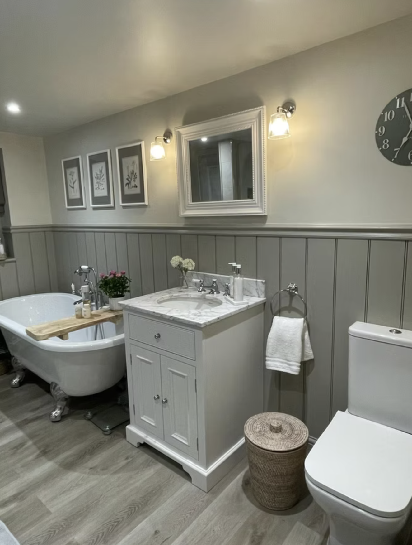 A roll-top bath, marble-topped vanity and painted tongue-and-groove panelling in a soft grey bathroom.