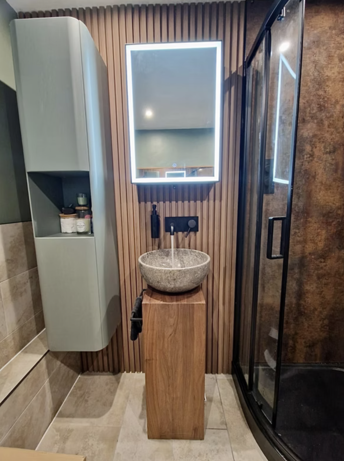 A pedestal basin with brass wall-mounted tap against slatted timber-effect porcelain.