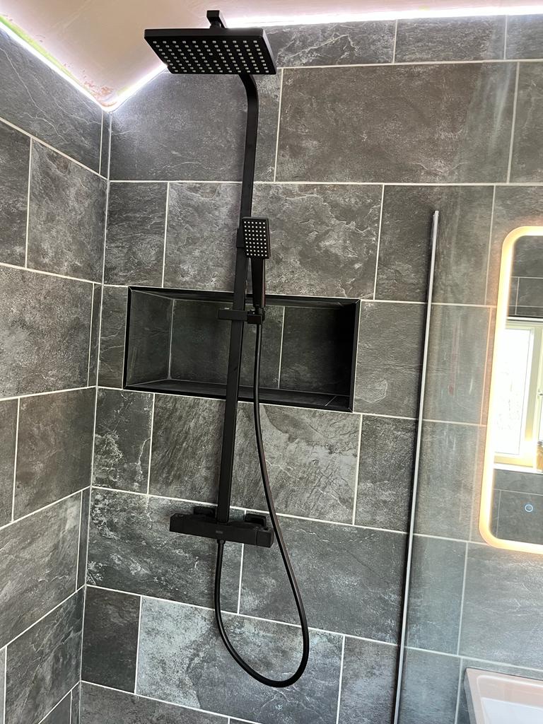 Matt black rainfall shower and recessed storage niche against slate-effect porcelain.